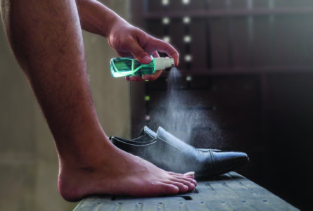 man using a small spray bottle of green liquid to spray his foot